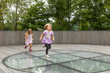 Two small children running across a deck made of wood and glass.