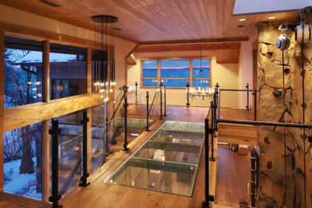 warmly lit modern home with wood, stone, and glass materials as well as glass flooring.