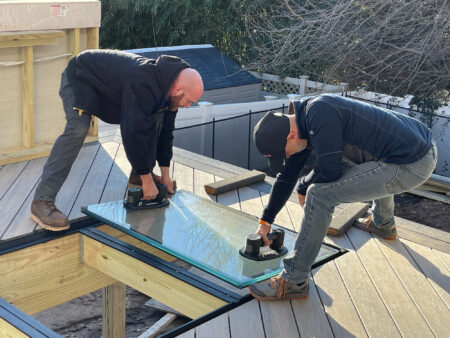 Two construction workers installing a modular glass decking system.