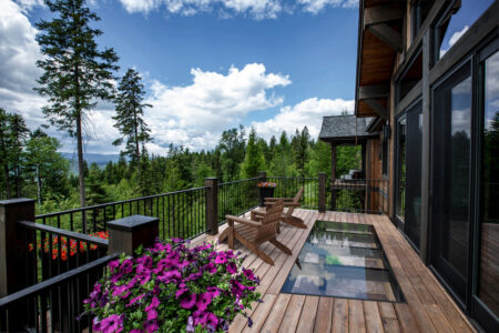 A beautiful wood and glass deck, with a view of pine trees and mountains.